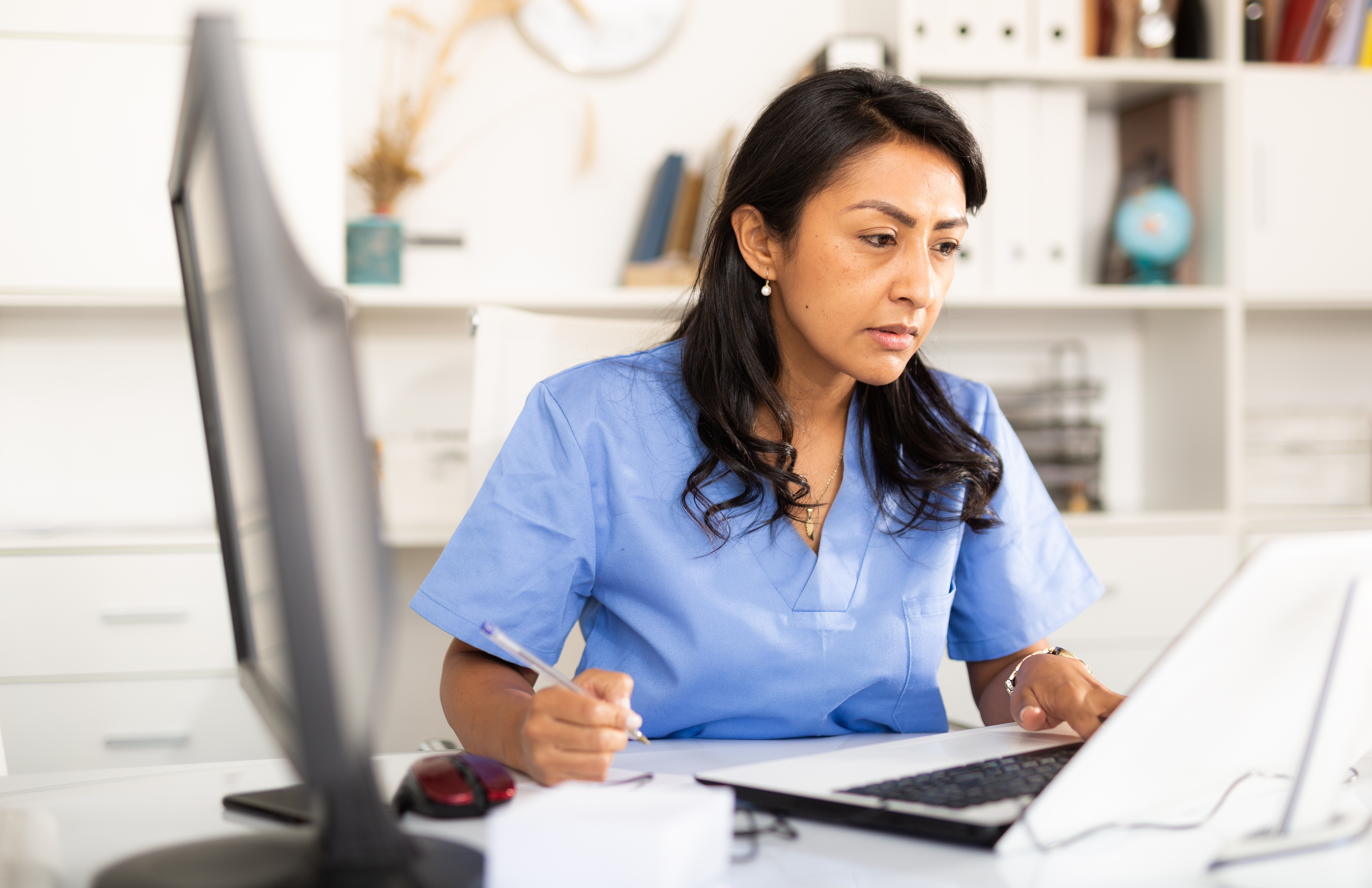 Doctor writing notes and reading something on laptop at her office